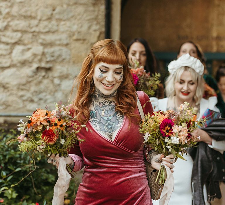 Bridesmaid in pink velvet bridesmaid dress with bouquets as she leads the bridal party to the ceremony 