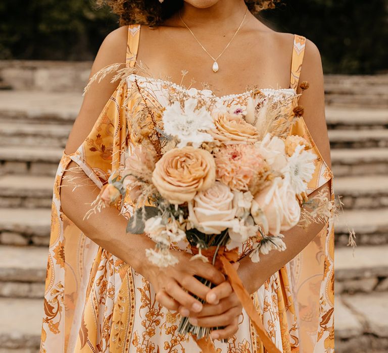 Bride carrying a neutral rose and dahlia flower bouuqet with colourful wedding dress 