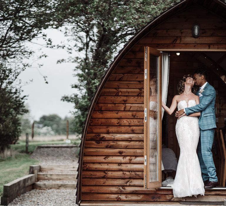 The bride and groom laugh by the outdoor cabins at Sedgewell Barn