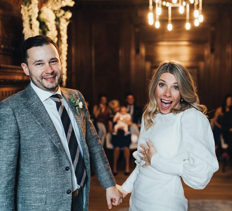 Happy bride and groom at Marylebone town hall wedding with chandelier, short bridal dress with puffy sleeves and groom wearing striped tie 