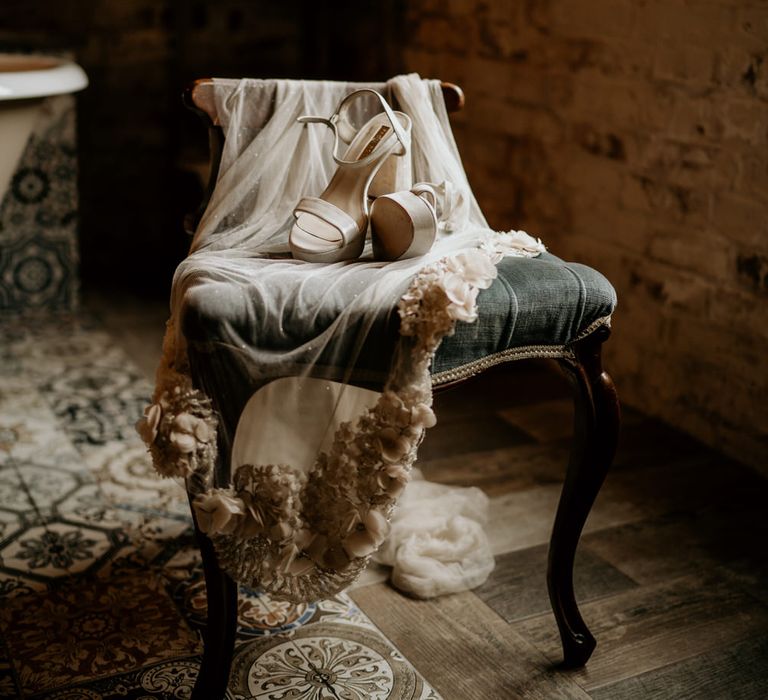 Beige wedding veil with flower applique detail and platform shoes draped over a velvet chair 