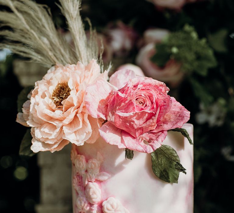 Close up of white and blush pink three tier wedding cake with rose, ranunculus and pampas grass decor