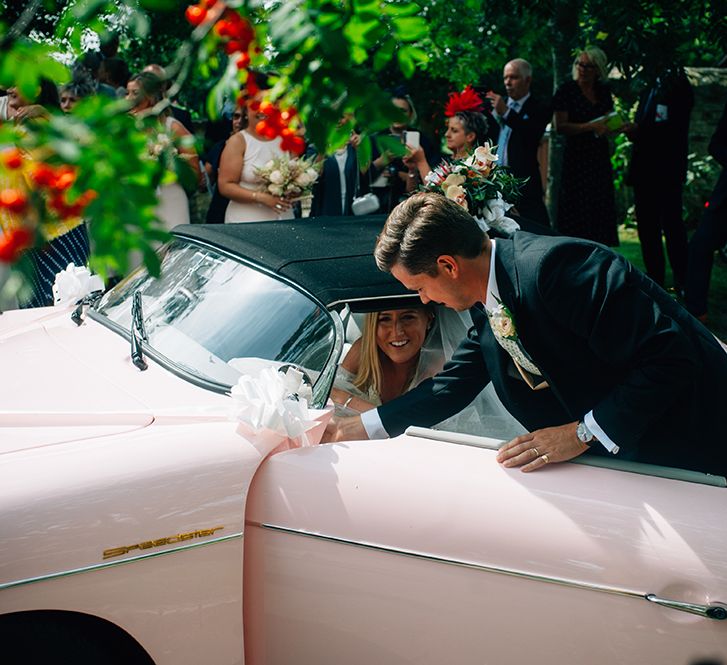 Bride sat in pink Porsche with her new husband holding the door at Cotswold wedding