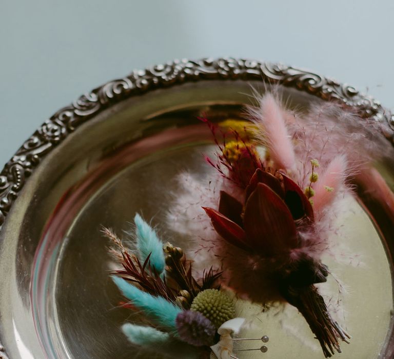 Pink and blue pampas grass button holes on decorative silver plate with intricate border