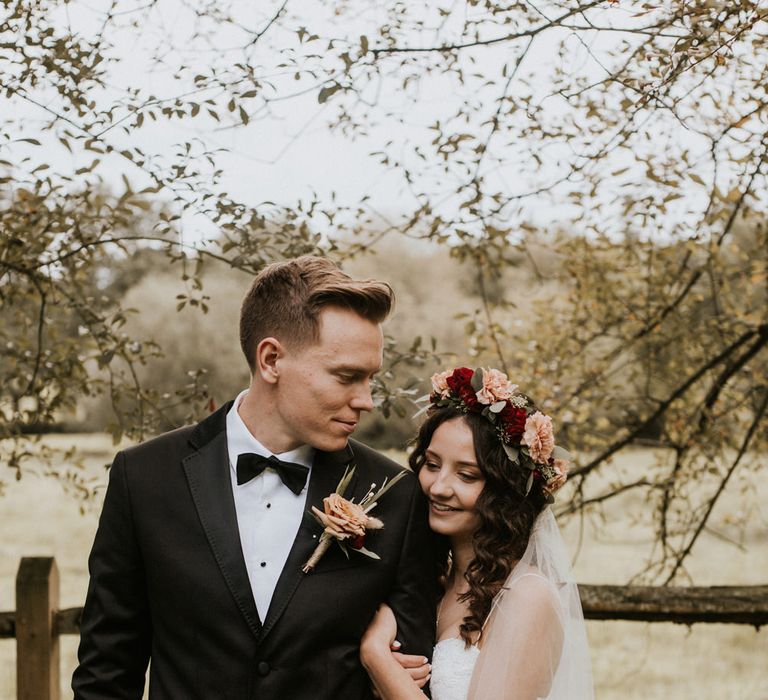 Bride in a ASOS wedding dress with flower crown embracing her husband in a black tuxedo 