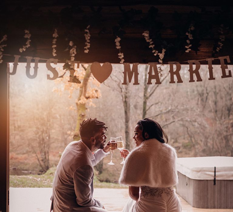 Bride & groom sit together underneath Just Married sign on decking 