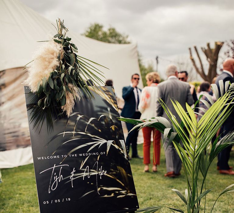 Black acrylic wedding welcome sign with white writing and pampas and palm leaf decor