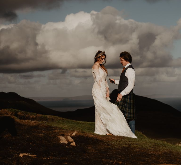 Bride & groom stand upon hillside with mountains in the background 