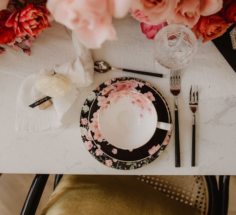 White tableware with black and pink floral design, silver and black cutlery and peach wedding flowers