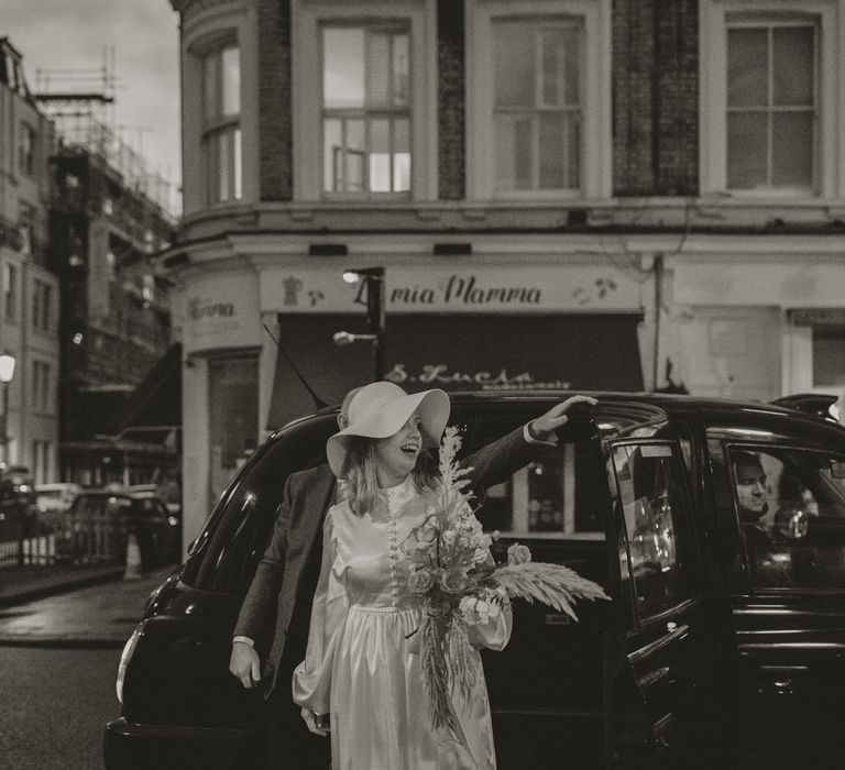 Bride leaves taxi in black & white image whilst holding floral bouquet