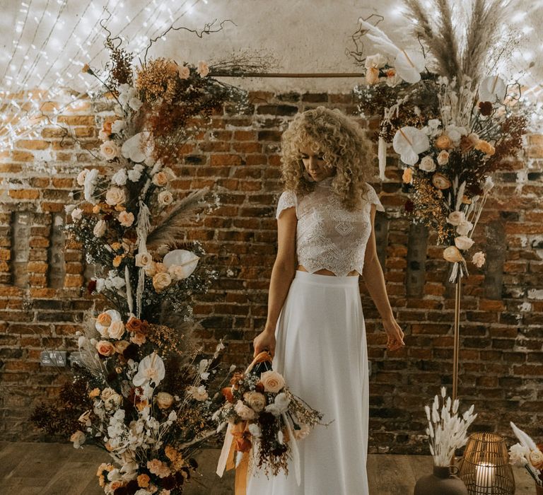 Bride with curly wedding hair standing in front of floral alter decorations of roses, anthuriums and pampas grass.