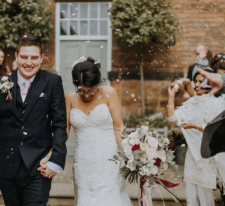 An Asian bride wearing Sophia Tolli holds her new husbands hand as they exit their ceremony. She holds an oversized rose bouquet.