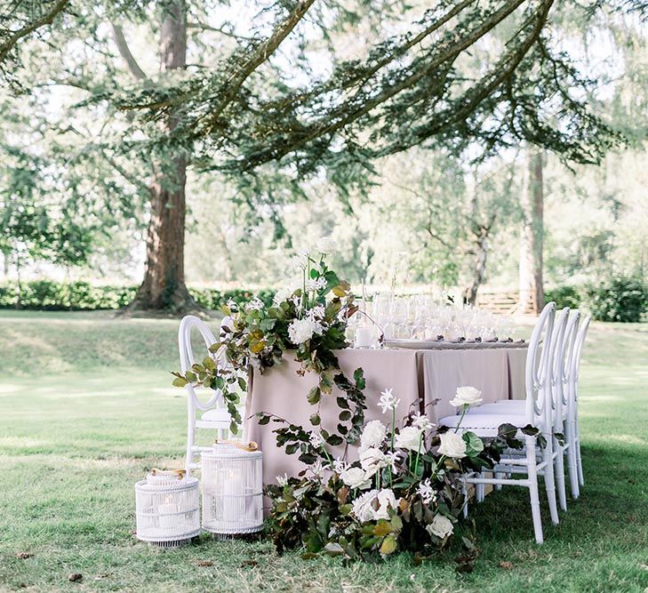 Intimate outdoor wedding reception table with linen tablecloth, white and green flower arrangements and white chairs 