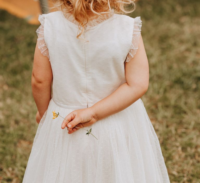 Girl in white dress holds flower behind her back at garden wedding reception