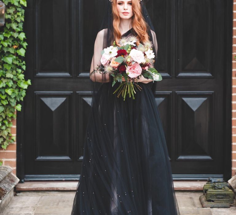 Bride with long auburn hair wearing a bridal crown holding a red, white and pink bouquet in a black tulle wedding dress 