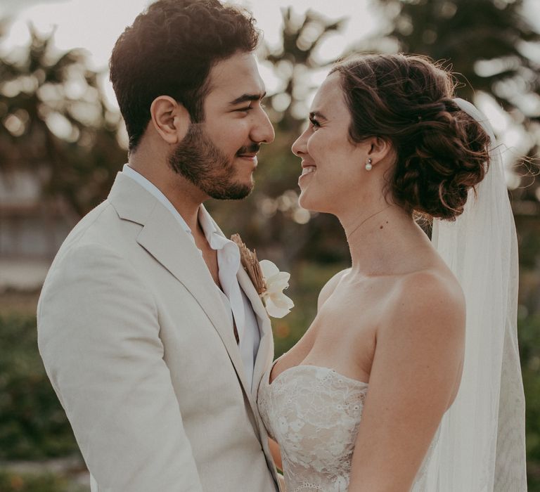 Bride & groom look lovingly at one another and hold hands as bride wears her dark hair in a low up-do