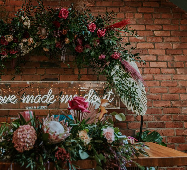 Neon lighting on wall in surrounded by brightly coloured florals and green foliage