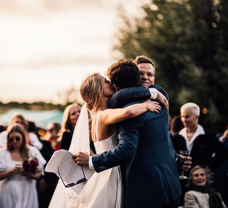 Bride and groom hug best man after wedding speech