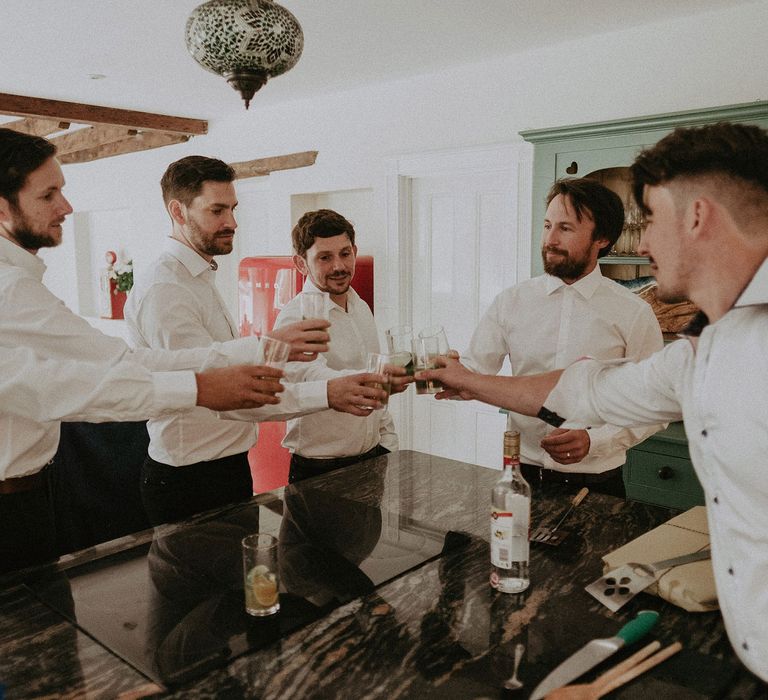 Grooms in white shits all clink glasses before Isle of Wight wedding with macrame wedding decor