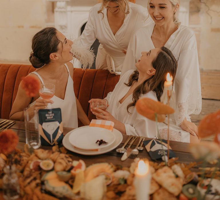 Bridal party gathered on the wedding morning in matching satin robes to enjoy a grazing breakfast and cocktails 