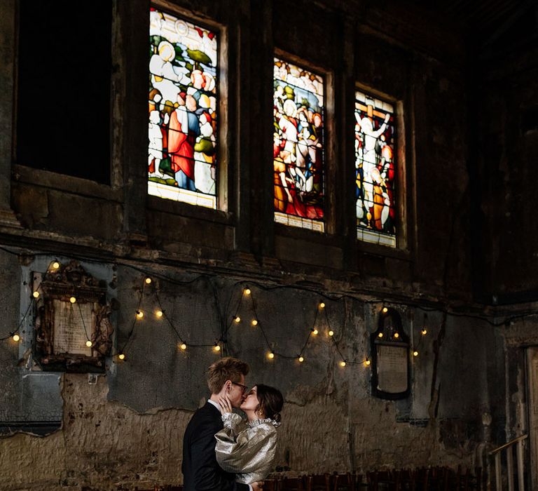 Bride and Groom kiss in empty Asylum London chapel expect from colourful art windows & fairy lights