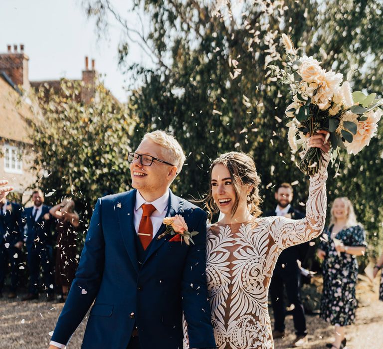 Groom in navy fitted suit & waist jacket with orange silk tie with Bride in Boho Long detailed wedding dress with bunny tails & pale pink roses bouquet 