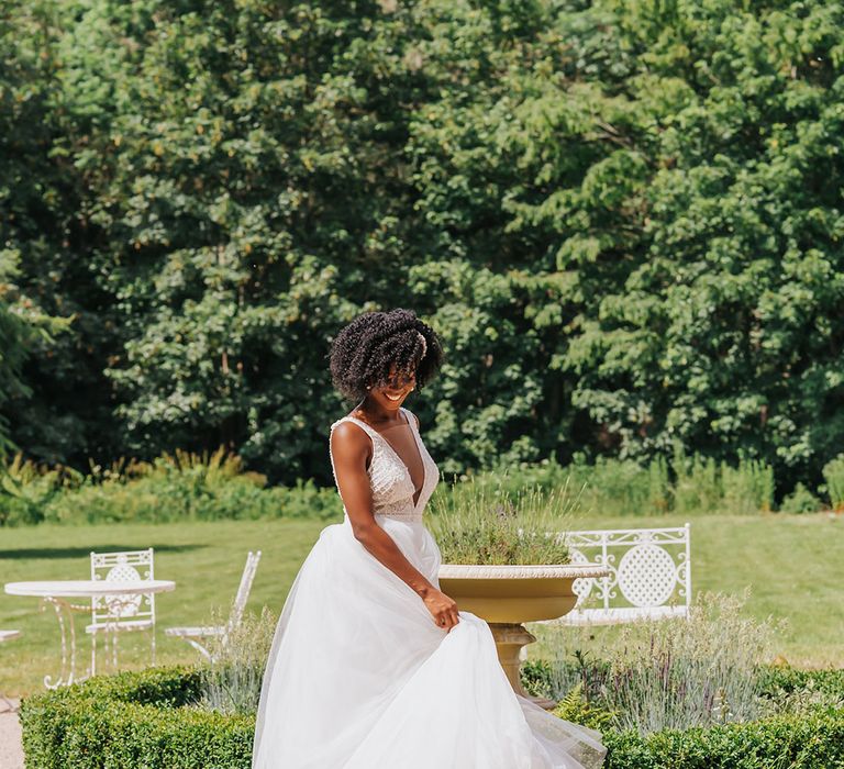 Black bride with short afro hair twirling her princess plunging neckline wedding dress with tulle skirt in the garden 