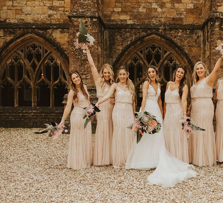 Bride stands with her bridesmaids who wear sparkly bridesmaid dresses and hold tropical bouquets 