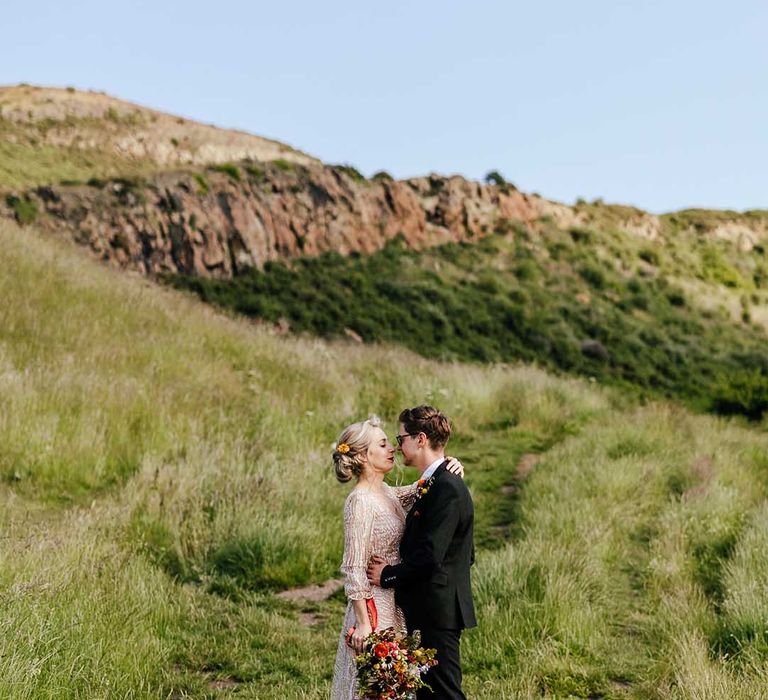 Bride & groom stand for couples portraits as bride wears sparkling gown complete with bright floral bouquet