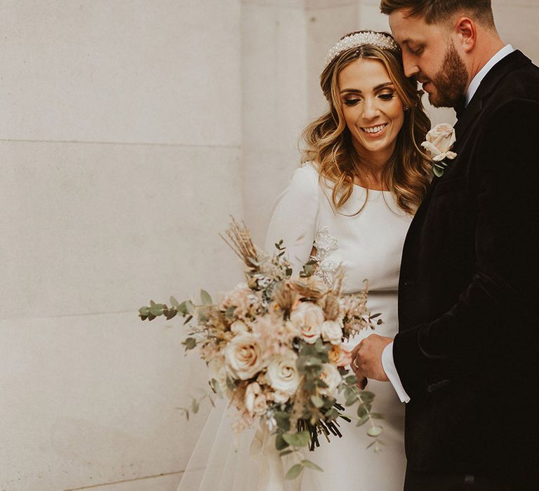 Bride and groom portrait with bride in a fitted wedding dress holding a pink flower and foliage wedding bouquet 