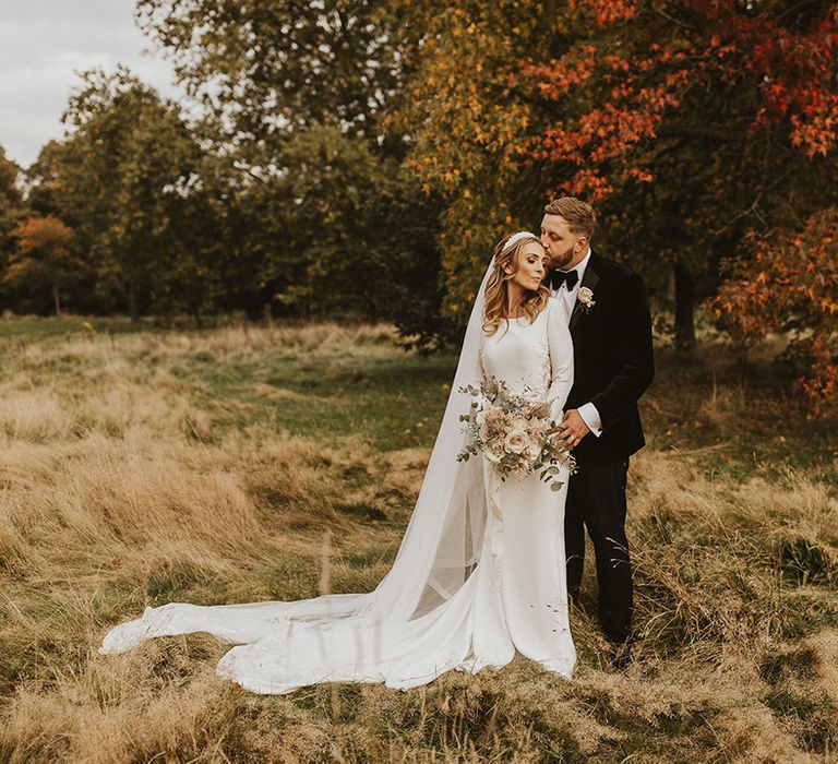 Black tie wedding with groom in a tuxedo and bride in a Pronovias fitted wedding dress in a field 