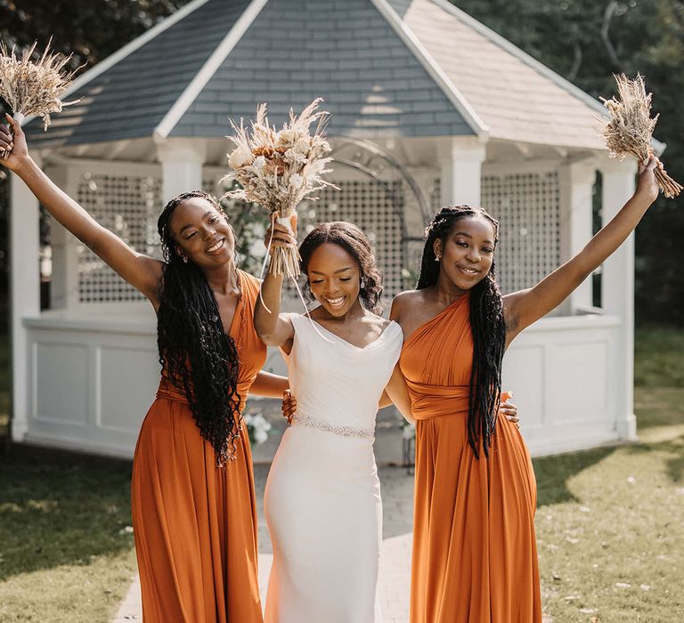 Bride stands with her bridesmaids who wear orange bridesmaids gowns