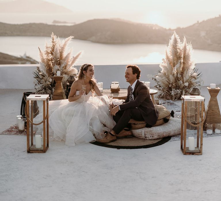 Bride & groom sit beside table on their wedding day outdoors 