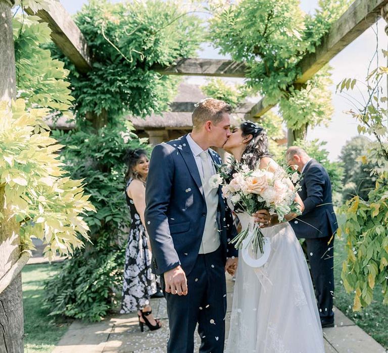 Bride & groom kiss under pergola on their wedding day