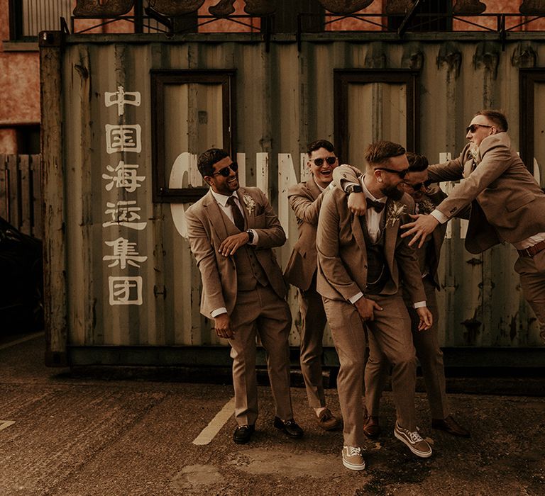 Fun groomsmen photography in front of an industrial container in tweed suits and trainers