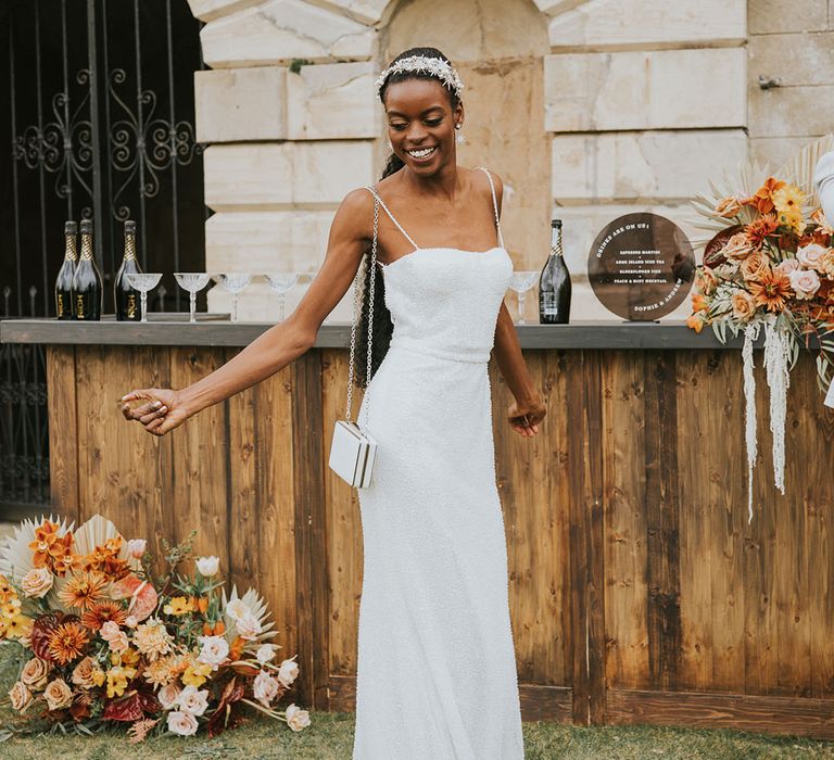 Black bride in a fitted beaded wedding dress with matching handbag and jewel encrusted headband dancing by the outdoor bar 