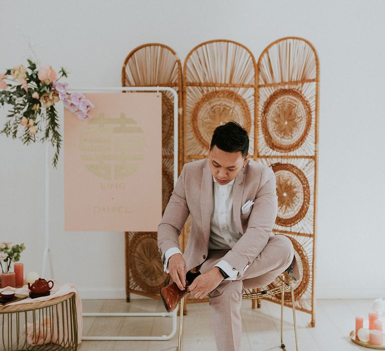 Groom in beige suit with tanned shoes with boutique of flowers with asian wedding decor 