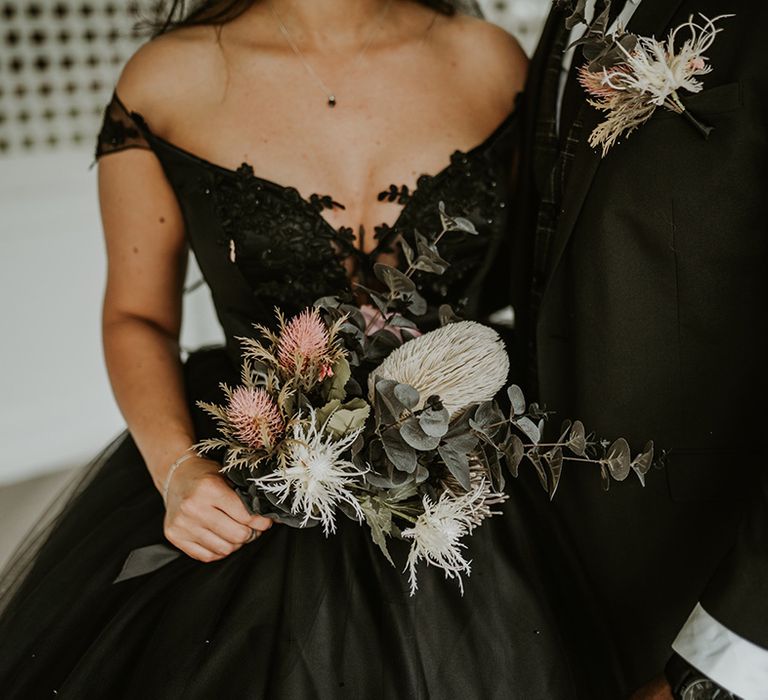 Bride wears homemade black wedding gown and holds floral bouquet 