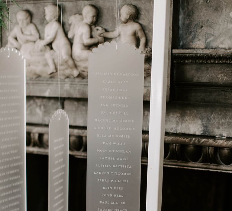 Frosted acrylic wedding seating chart hanging from a metal frame