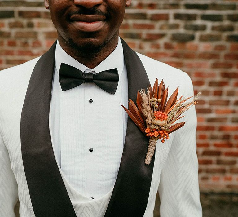 White tuxedo with bow tie and orange buttonhole for groom