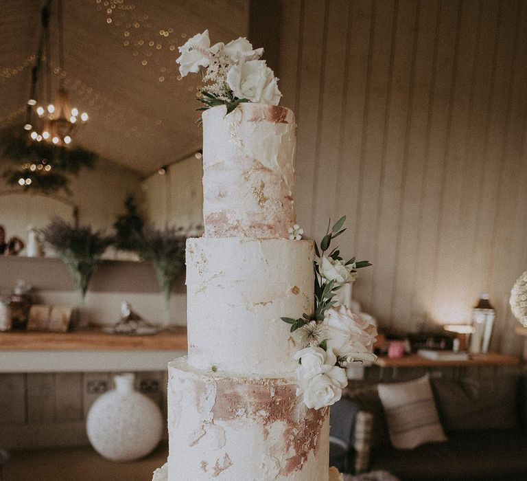 Four-tier wedding cake with white, pink and gold frosting with white roses for decoration