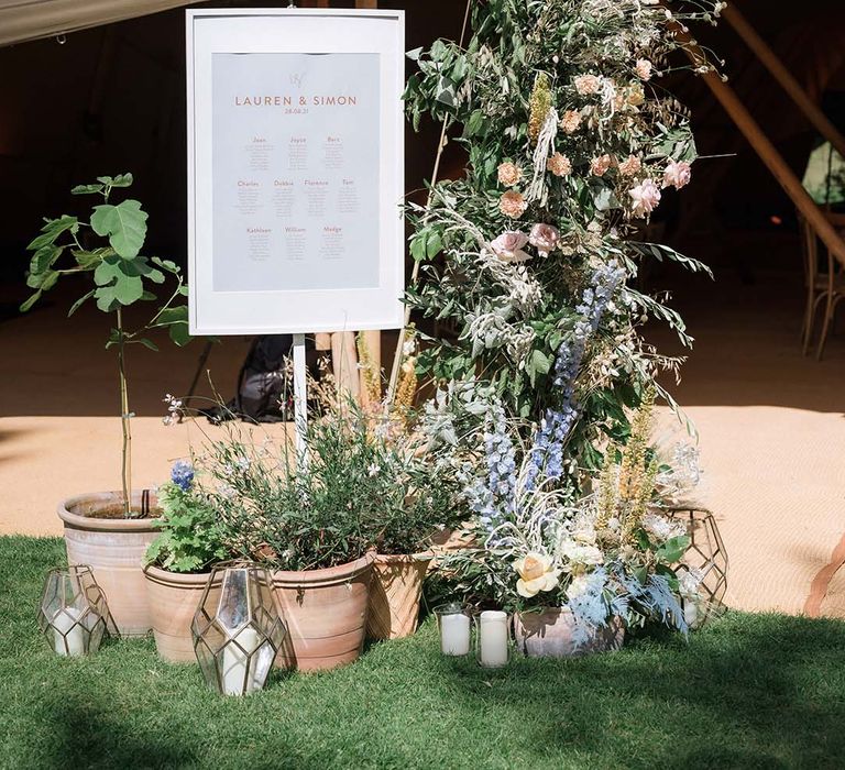 White and pink wedding seating/table chart with large pastel flower display and potted plants with candles in lanterns 