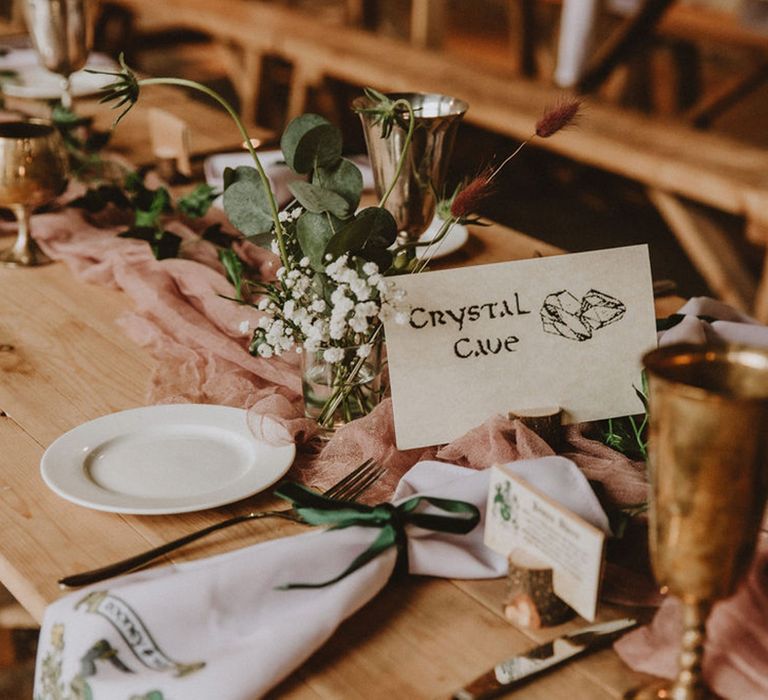 Table name cards with medieval font and pictures with sheer pink table runner, golden goblets and personalised name cards with the guests' surname and coat of arms