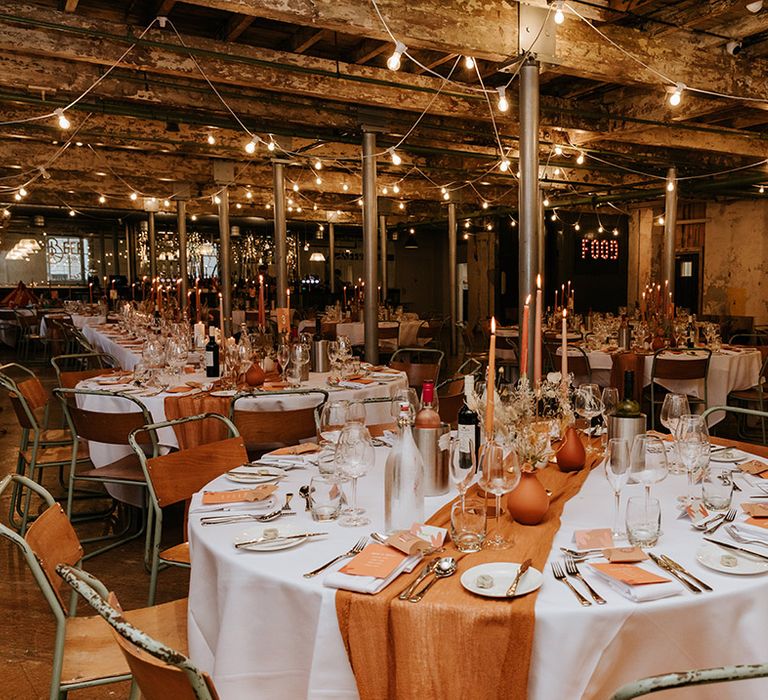 Table settings for autumnal wedding with orange and warm brown coloured vases, candles, runners, napkins and flowers