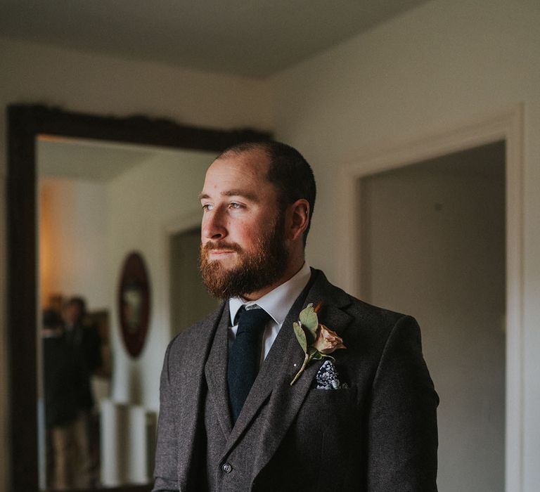 Groom in three piece dark grey suit with patterned handkerchief and toffee rose boutonnière