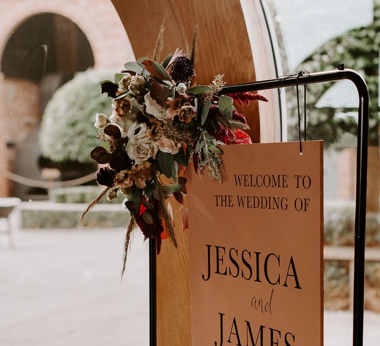 Hanging orange welcome wedding sign with orange and deep red autumnal flower arrangement