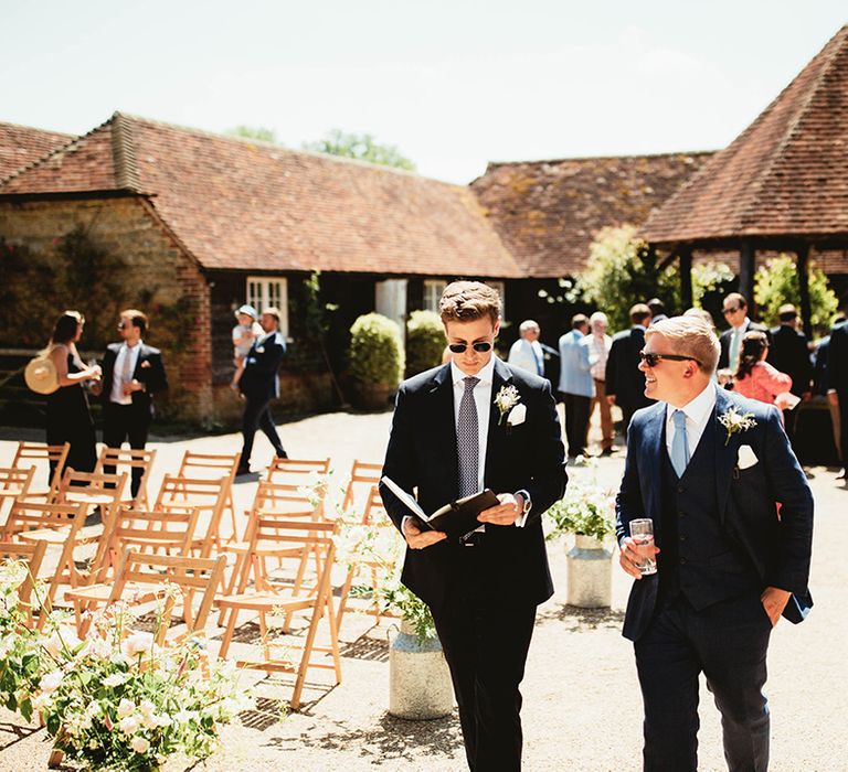 Groom in blue suit and sunglasses walks with wedding celebrant also in sunglasses for outdoor wedding ceremony