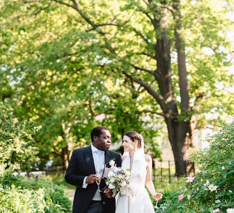 Bride and groom smile at each other holding champagne glasses on their wedding day