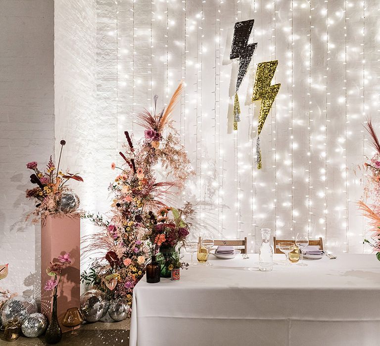 Sweetheart top table for bride and groom with fairy light backdrop with lightning decor and colourful flowers as well as disco balls