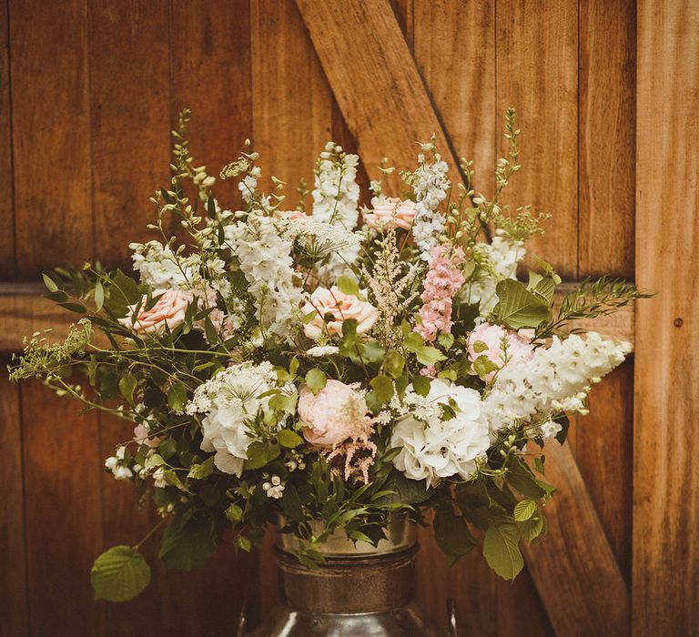 White and pink wedding flowers in vintage silver milk churn including stock, hydrangeas, and roses